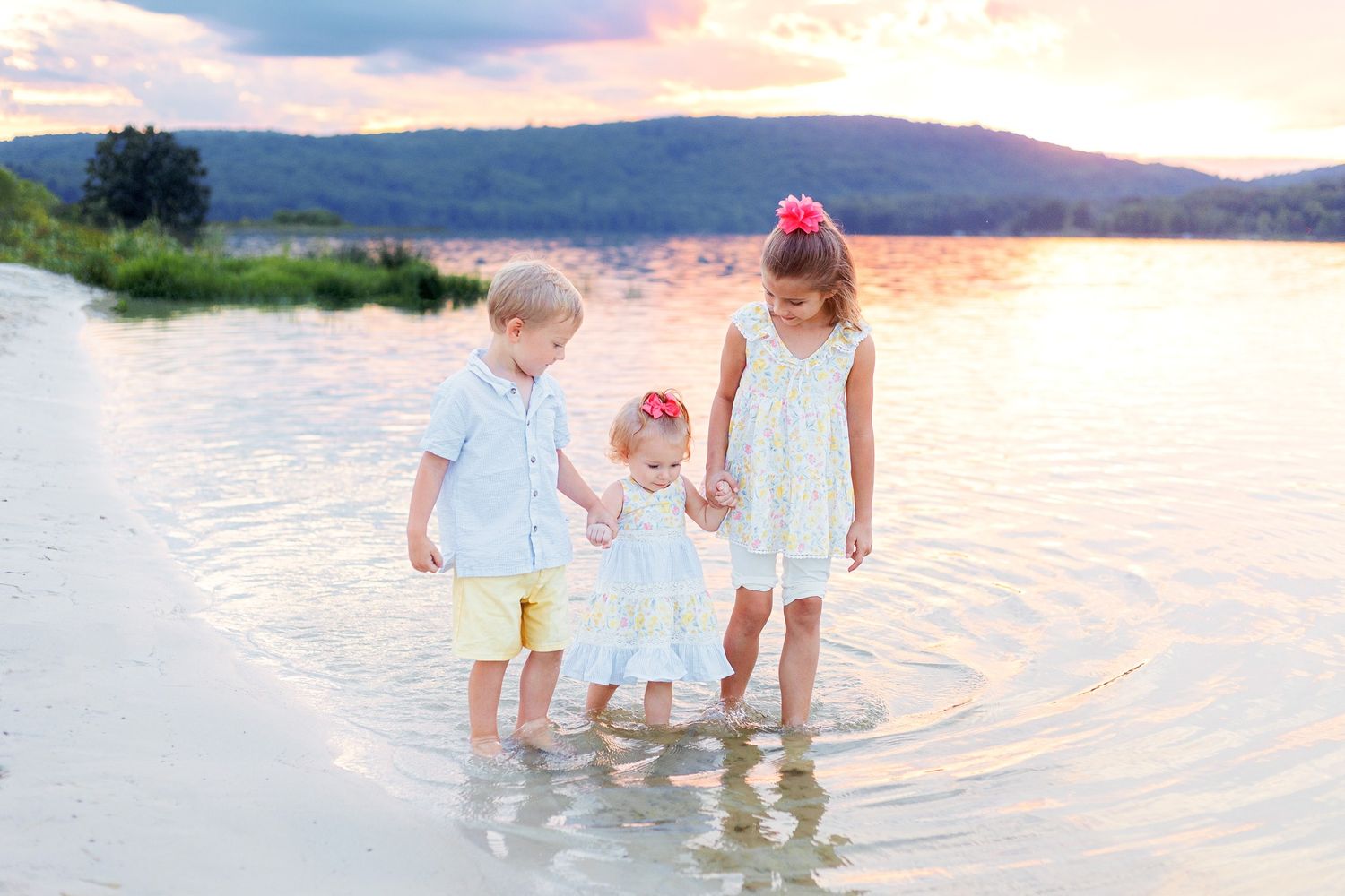 Children play together in shallow waters at sunset as ripples form around their feet near a mountainous shoreline.
