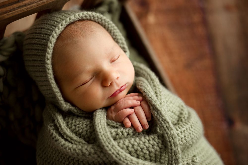 Peaceful sleeping newborn wearing knit bonnet nestled in green blanket.