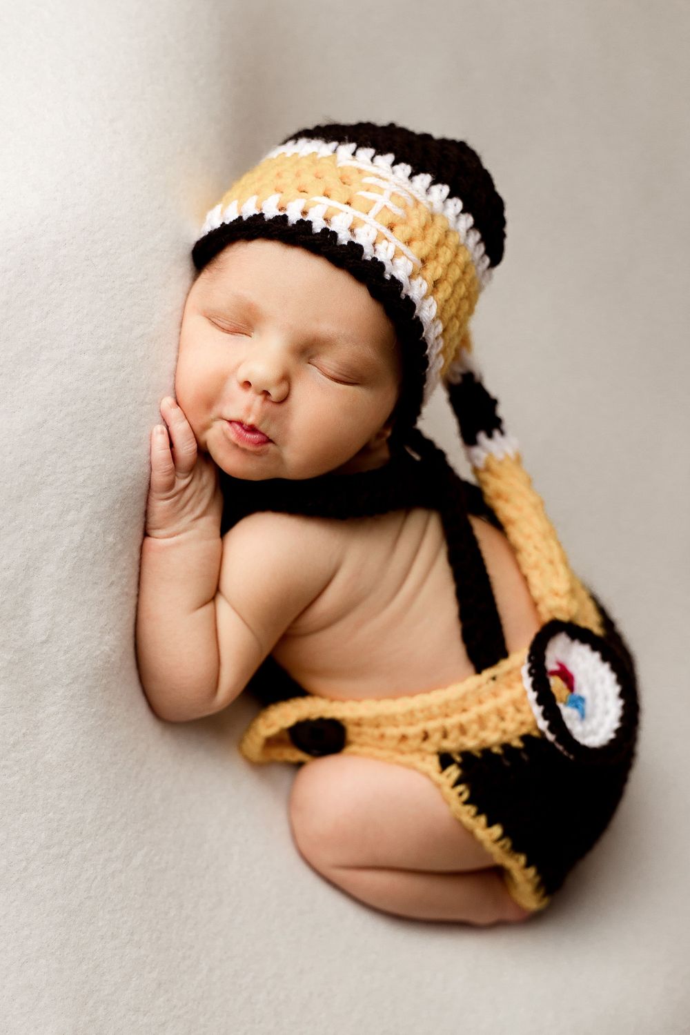 Newborn baby in black and yellow knit hat and diaper cover sleeping during studio photoshoot.