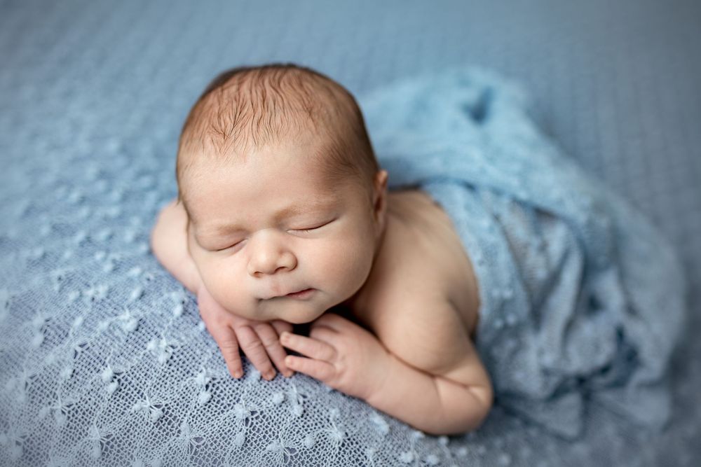 Peaceful sleeping newborn baby wrapped in soft blue blanket during professional photography session.