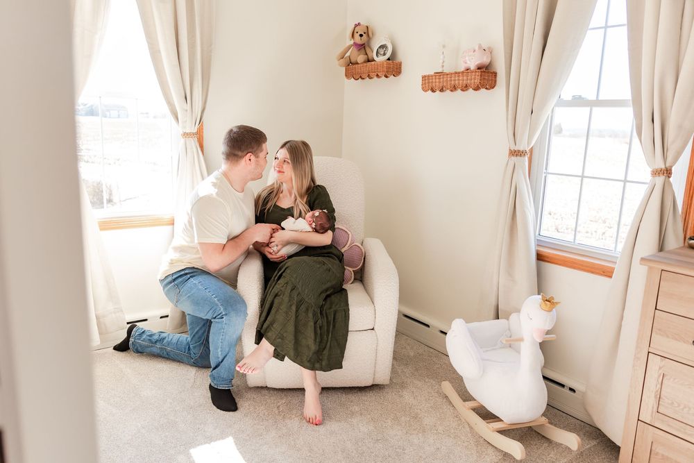 A couple shares an intimate moment while sitting together in a cozy nursery corner with soft curtains and decor.