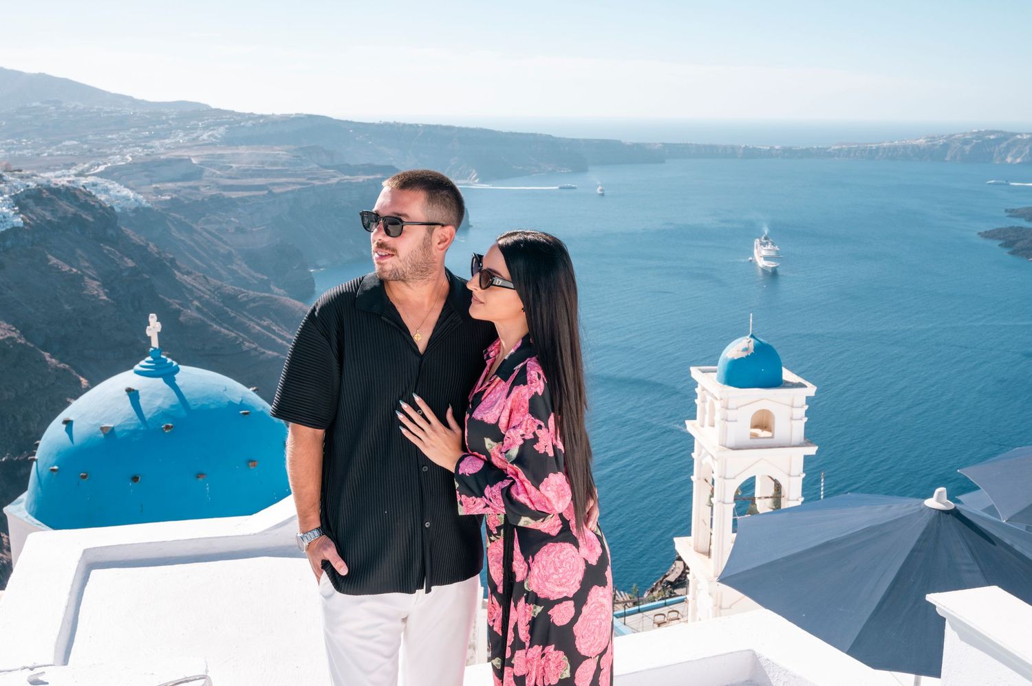A couple poses against Santorini's famous blue dome churches with the Aegean Sea in the background.