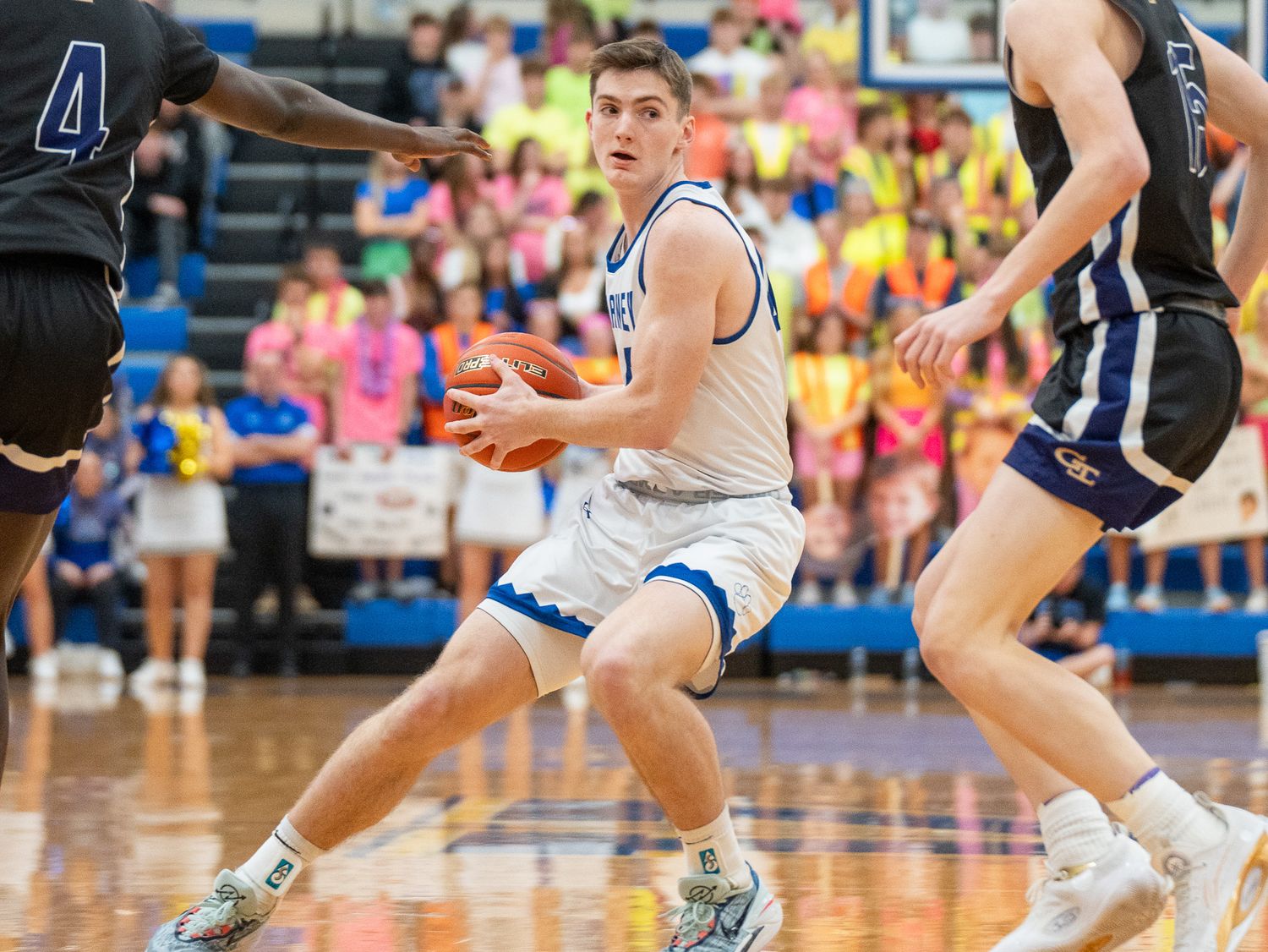 Basketball player drives toward basket on polished court during competitive game action.