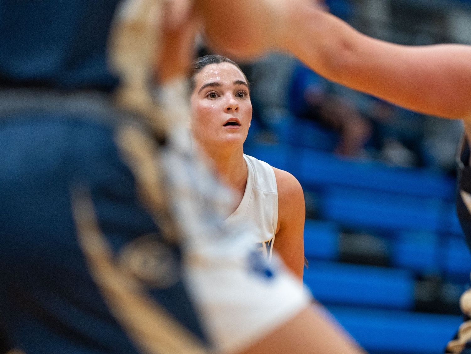 Player intently watches action during basketball game in gymnasium.