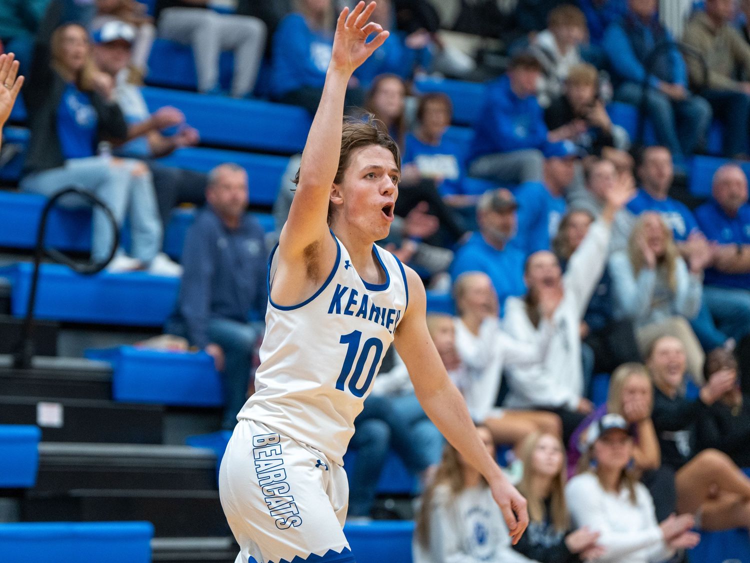 Basketball player celebrates after scoring during game in packed gymnasium.