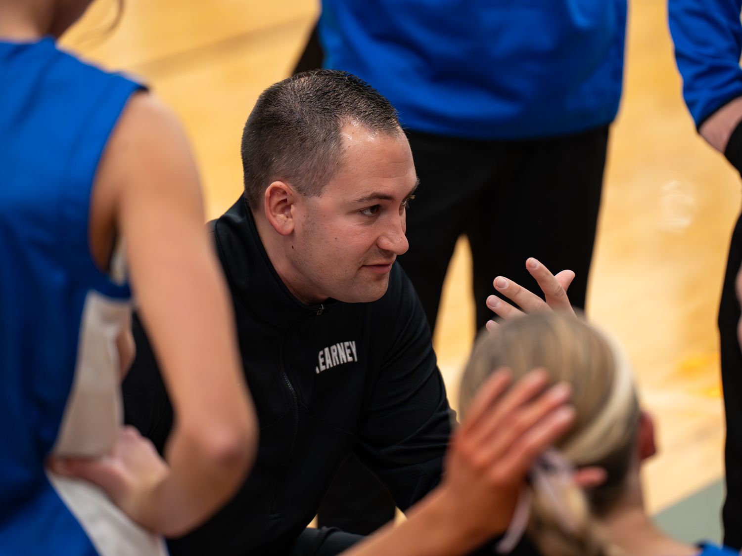 Basketball coach gives instructions during timeout on gymnasium sideline.