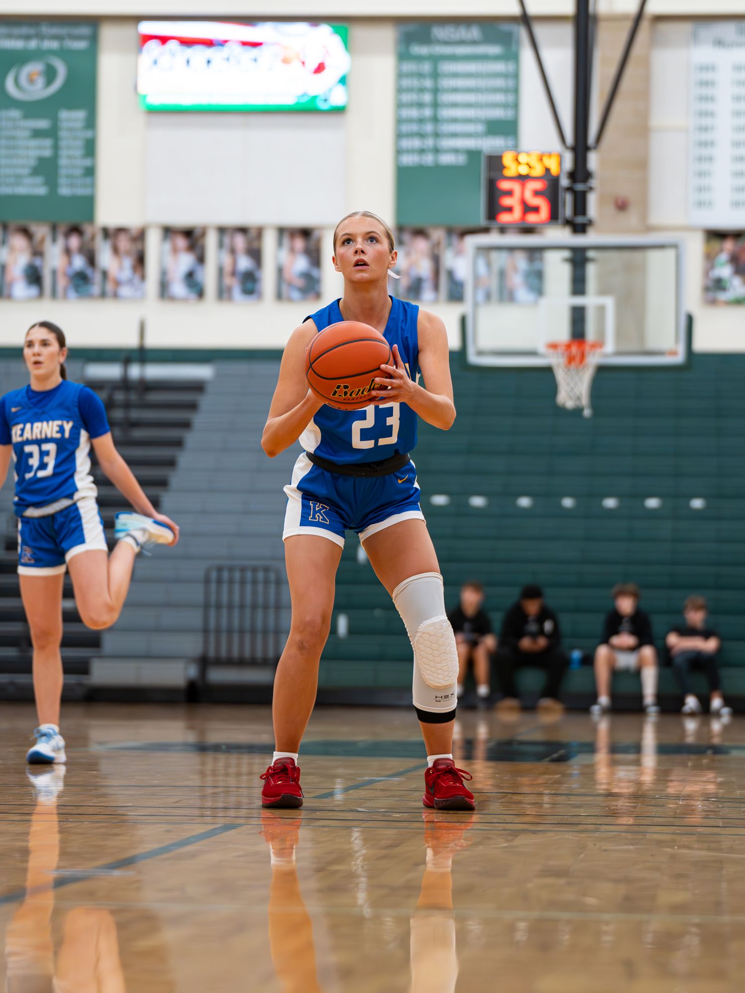 Basketball player in blue Kearney uniform number 23 prepares to shoot free throw on court.