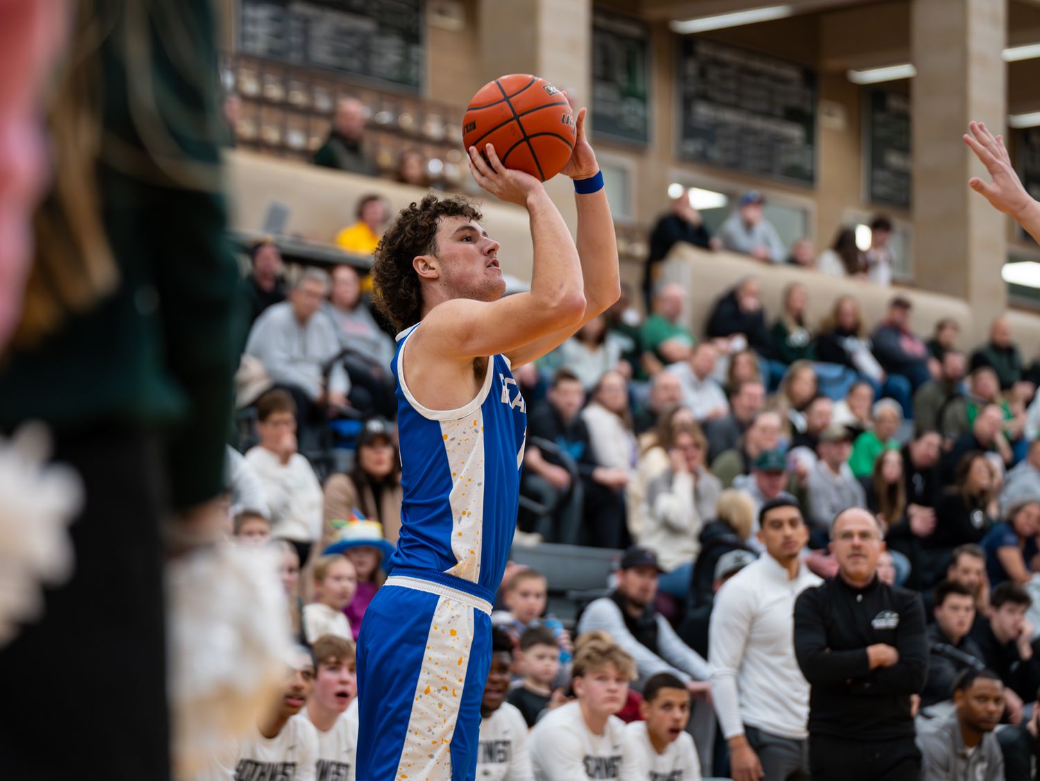 Basketball player in blue jersey takes jump shot during competitive game.