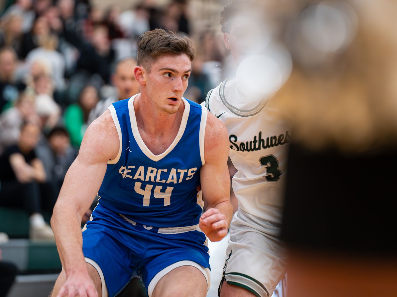 Player number 44 in blue Bearcats uniform positions for play during basketball game.