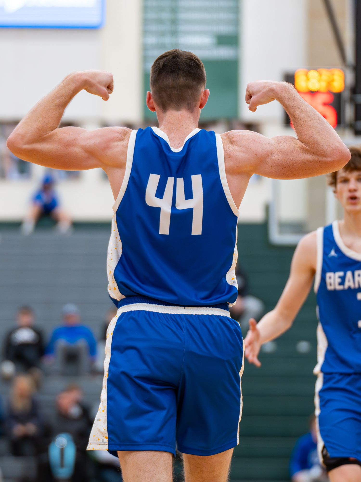 Basketball player in blue jersey number 44 flexes muscles showing back to camera.