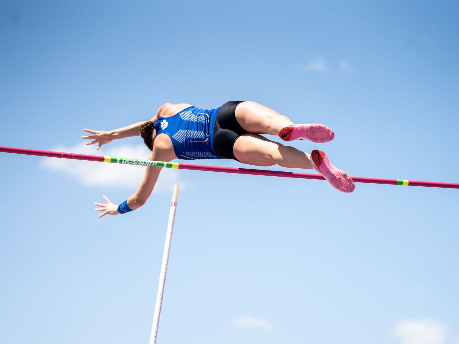 Athlete performing high jump over red bar against blue sky background.