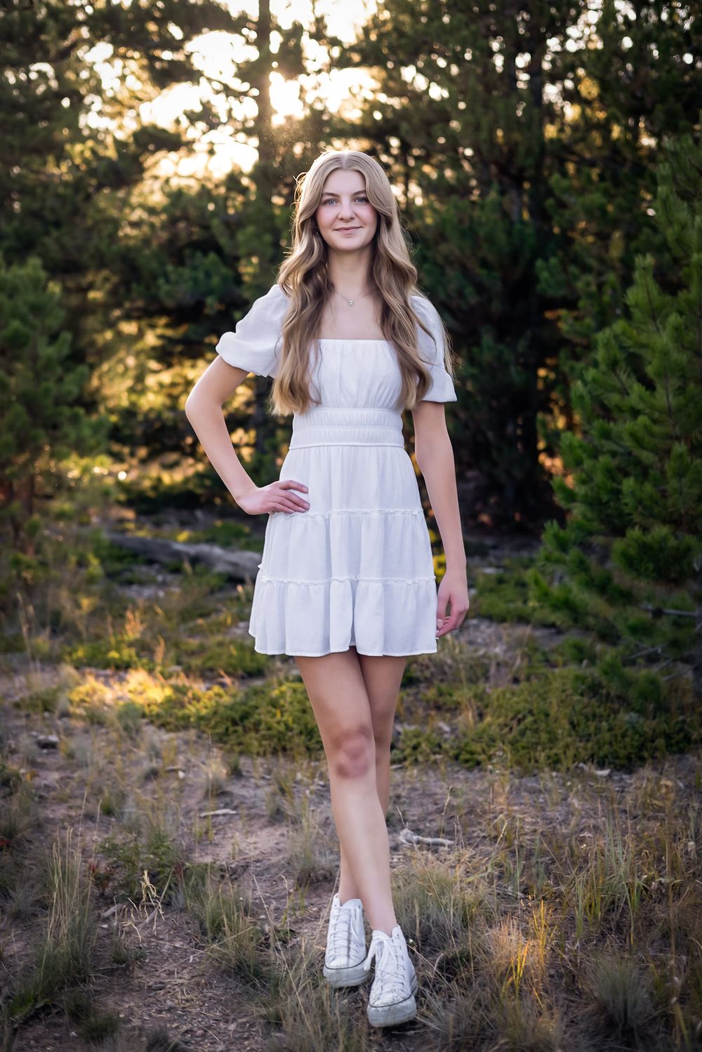 Person in white dress poses on nature trail during golden hour.