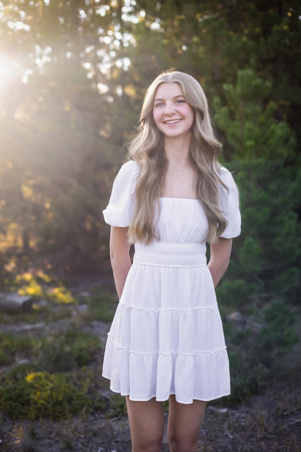 Person wearing white summer dress poses in sunlit outdoor setting.