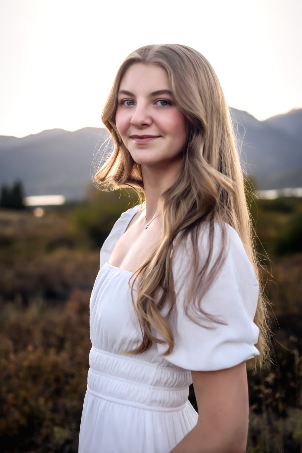 Portrait in a white dress against mountains at golden hour creating a dreamy outdoor setting.