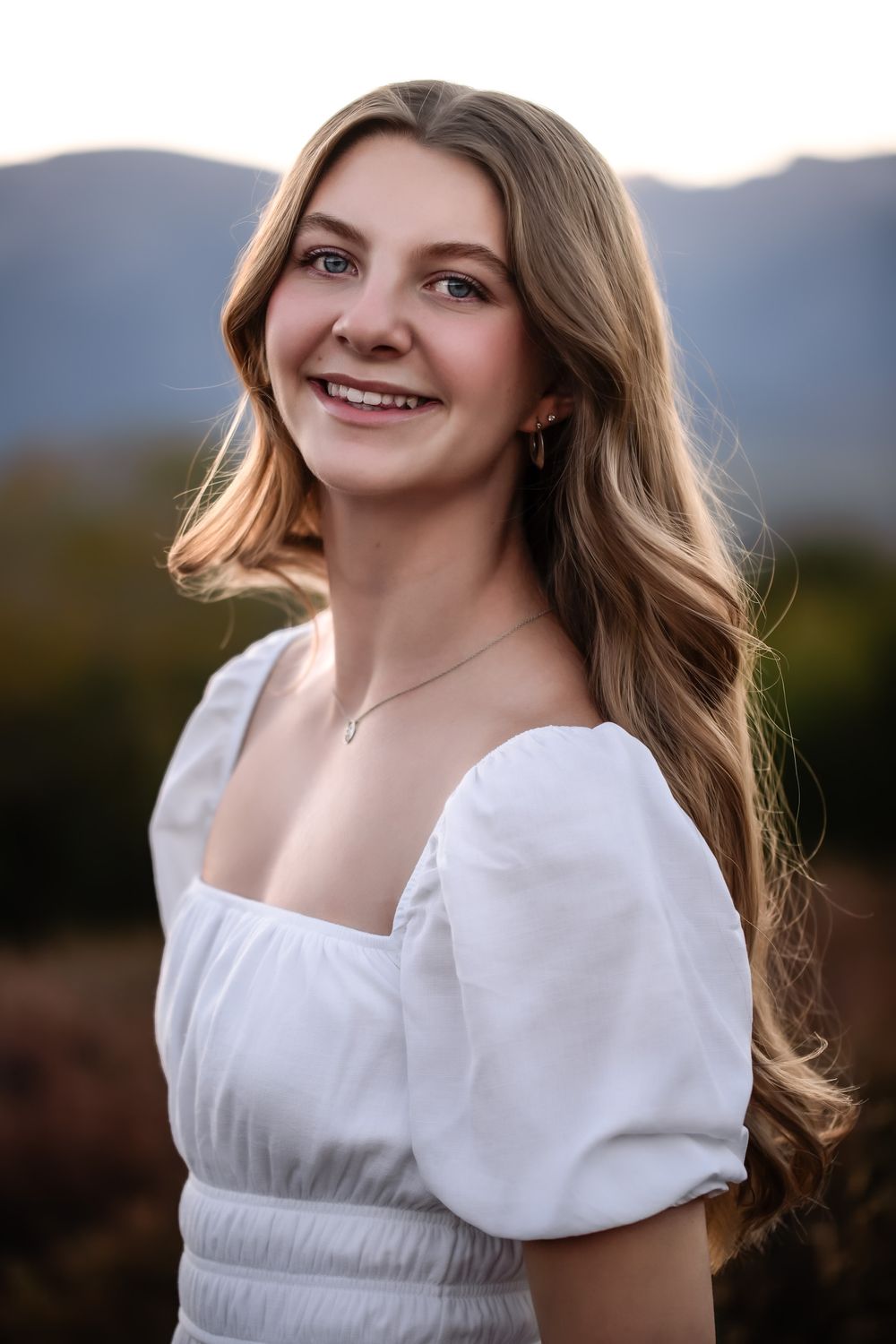 Close-up shot in white dress with soft natural lighting and mountain backdrop.