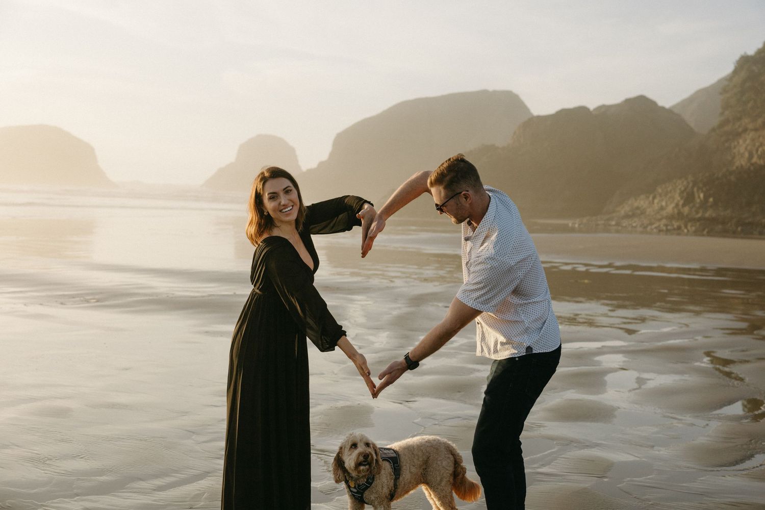 A couple dancing together on a misty beach at sunset with their dog watching beside them.