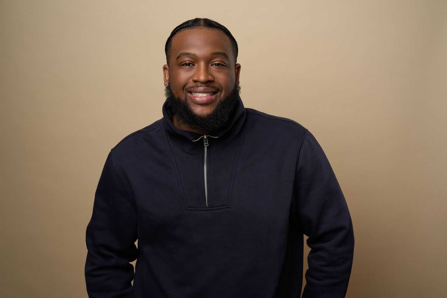 Professional headshot against beige background wearing black quarter-zip pullover.