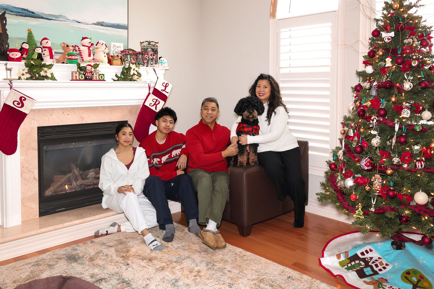 Family around a Christmas tree and fireplace with their family dog, posing for a photo