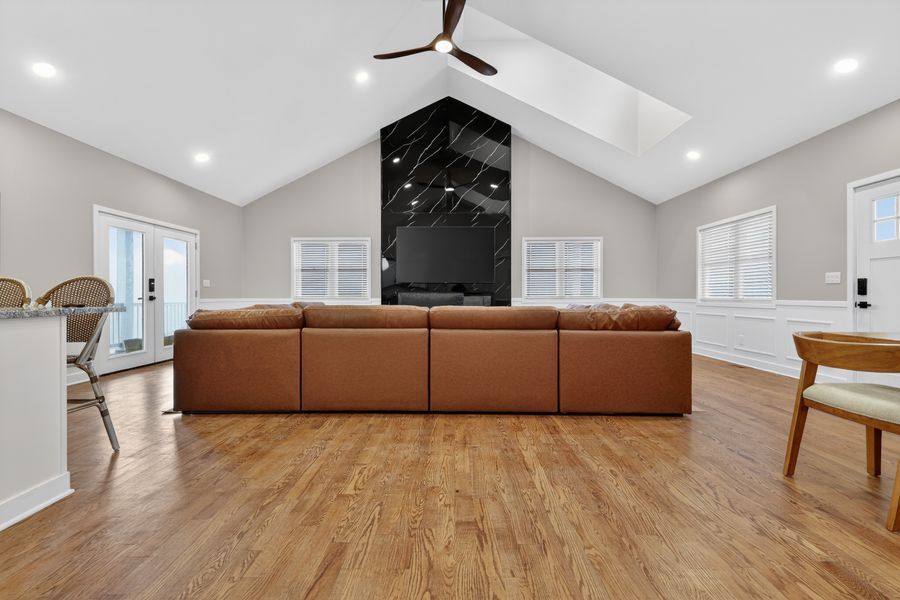 Spacious living room with vaulted ceiling, brown leather sectional sofa, hardwood floors, and modern black fireplace.