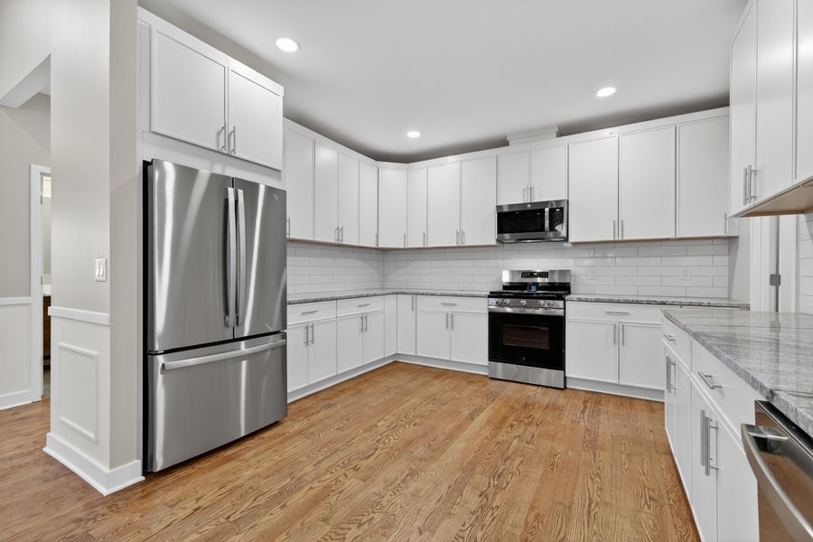 Modern kitchen with white shaker cabinets, stainless steel appliances, marble backsplash, and hardwood floors.
