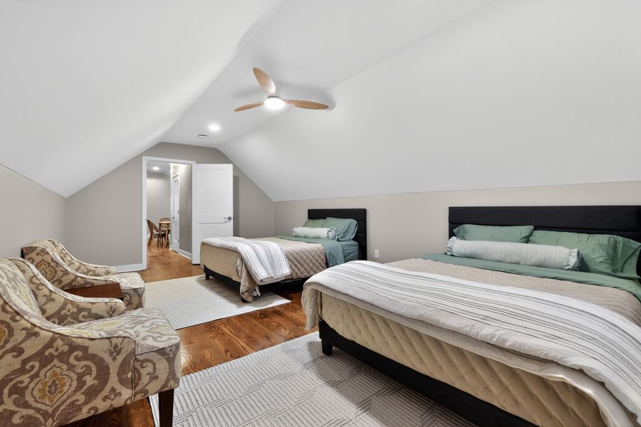 Spacious attic bedroom with vaulted ceiling, ceiling fan, two beds, and hardwood floors.