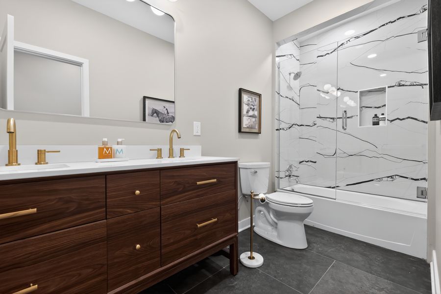 Modern bathroom with dark wood double vanity, gold fixtures, marble shower surround, and dark tile floors.