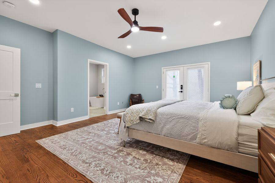 Large master bedroom with blue walls, hardwood floors, ceiling fan, and French doors leading to outdoor space.