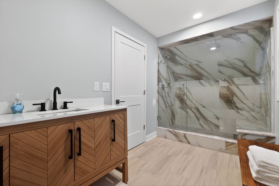 Modern bathroom featuring a wood vanity with black fixtures and a marble-tiled walk-in shower with glass doors.