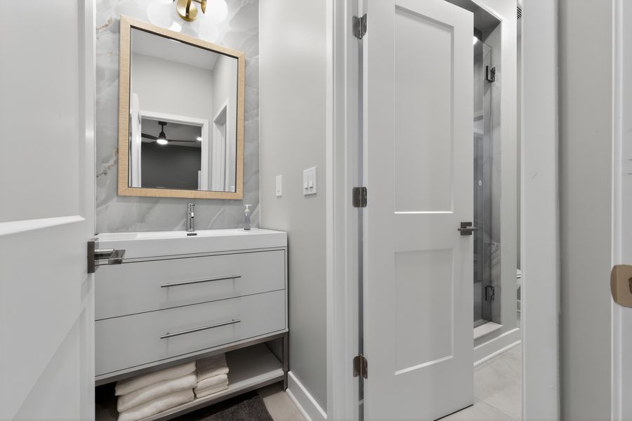 Elegant bathroom vanity with white cabinet, gold-framed mirror, and marble tile backsplash.