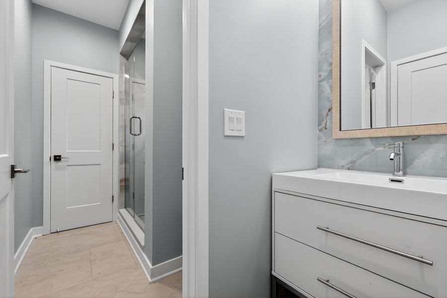 Bright bathroom featuring white floating vanity, marble backsplash, and glass-enclosed shower.