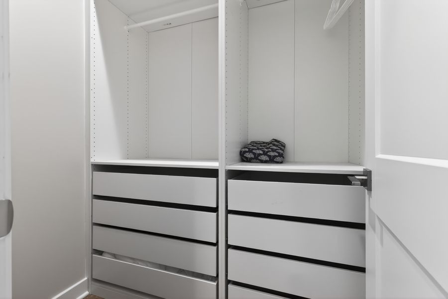 Modern white walk-in closet with built-in shelving, black-handled drawers, and hanging rods for organized storage.
