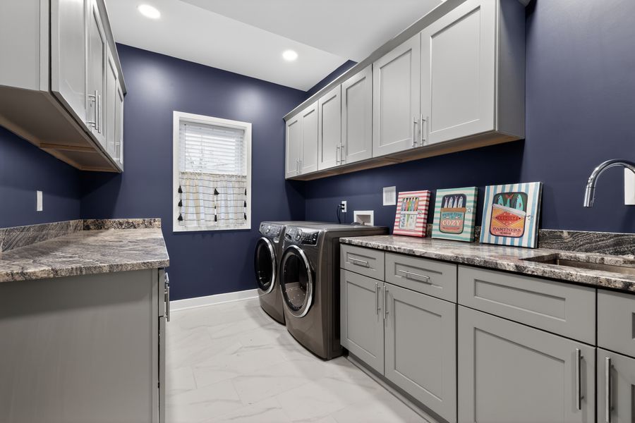 Modern laundry room with gray cabinets, navy blue walls, front-load washer and dryer, and granite countertops.