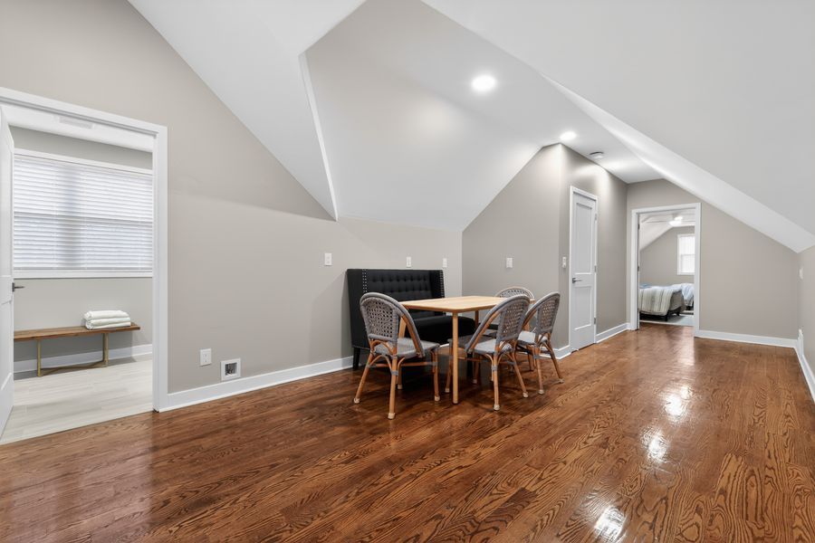 Bright attic dining area with vaulted ceilings, gleaming hardwood floors, a small table with chairs, and a cozy reading nook.