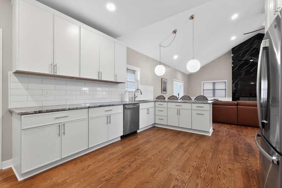 White kitchen with subway tile backsplash, granite counters, stainless steel appliances, and hardwood floors.