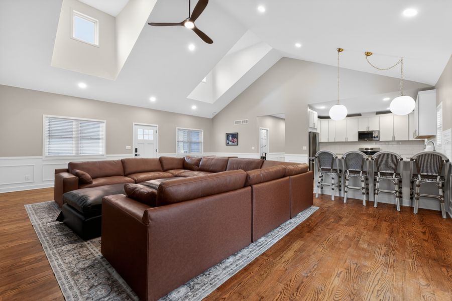 Spacious open-concept living room with vaulted ceiling, brown sectional sofa, hardwood floors, and kitchen bar seating.