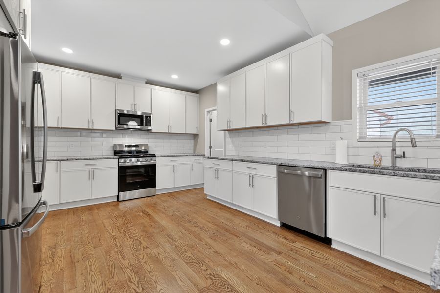 Modern white kitchen featuring stainless steel appliances, granite countertops, subway tile backsplash, and light hardwood floors.