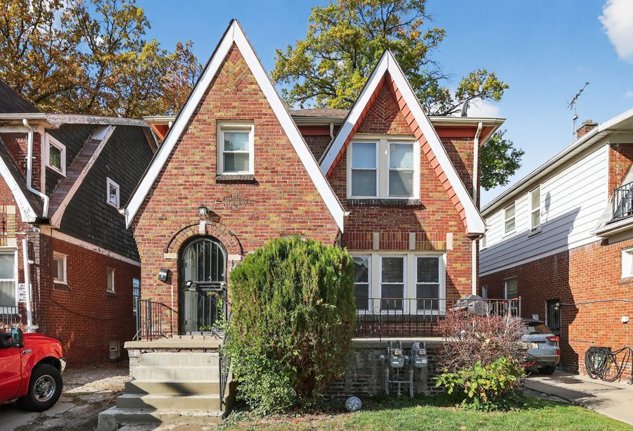 Charming red brick Tudor-style home with steep gabled rooflines, arched entry, and mature trees in a residential neighborhood.