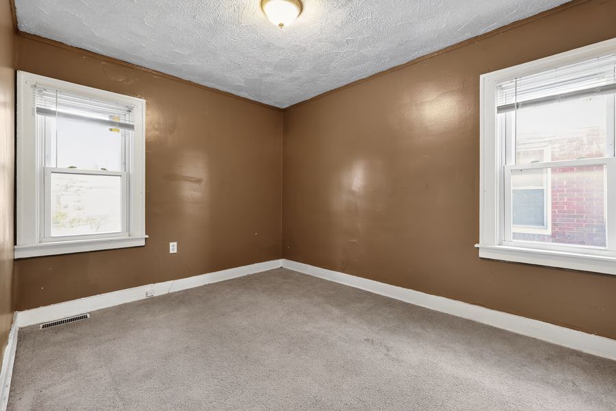 Empty bedroom with neutral carpet, brown walls, two windows, and textured ceiling in a residential home.