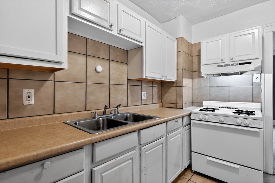 White kitchen cabinets with tile backsplash, double sink, and white gas range in a cozy apartment kitchen.