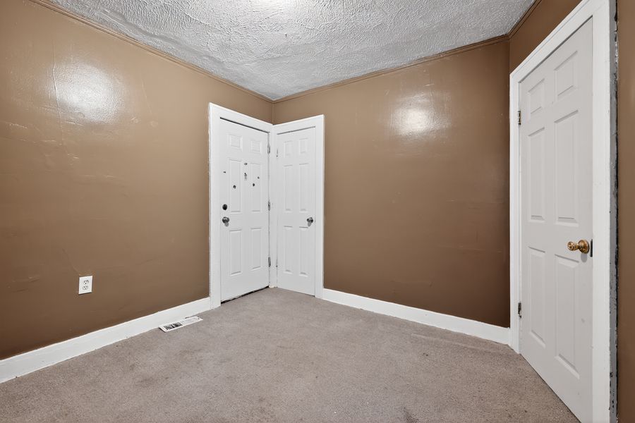 Empty carpeted bedroom with beige walls, white doors, and textured ceiling in a residential home.