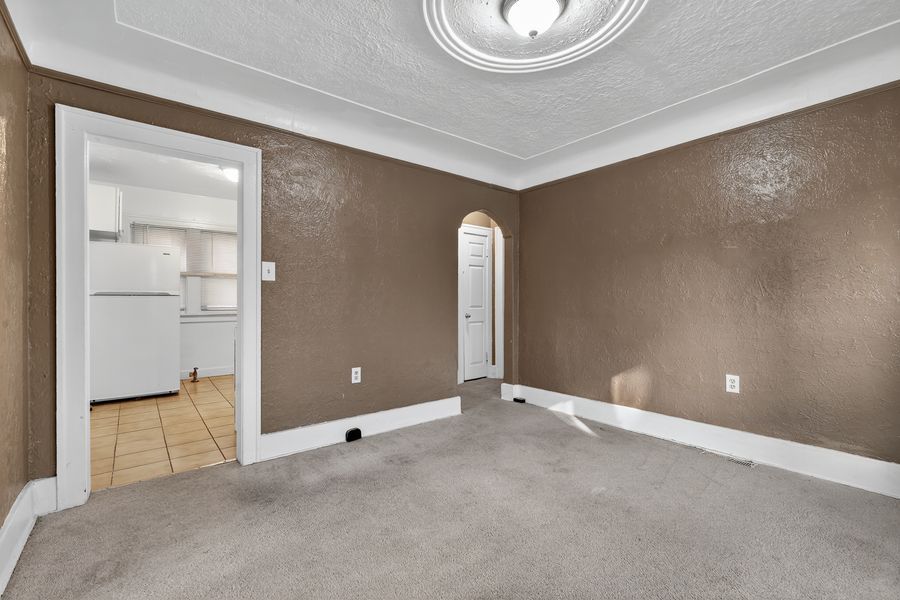 Spacious bedroom with gray carpet, brown walls, crown molding, and arched doorway leading to kitchen.