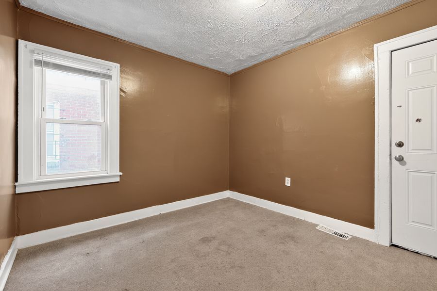 Empty room with tan walls, white trim, beige carpet, a single window, and a white door in a residential home.