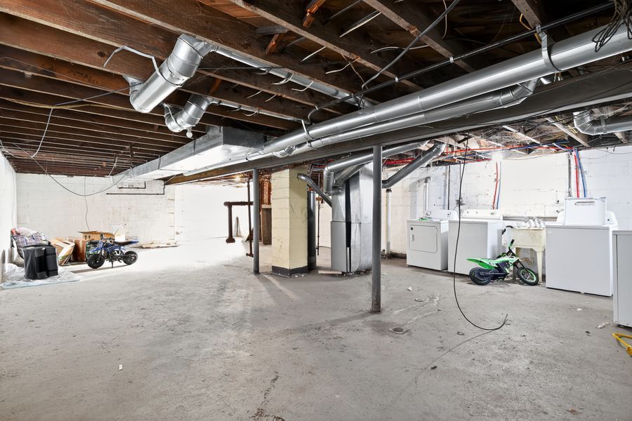 Unfinished basement with exposed ductwork, concrete floors, and utility appliances including washer and dryer.