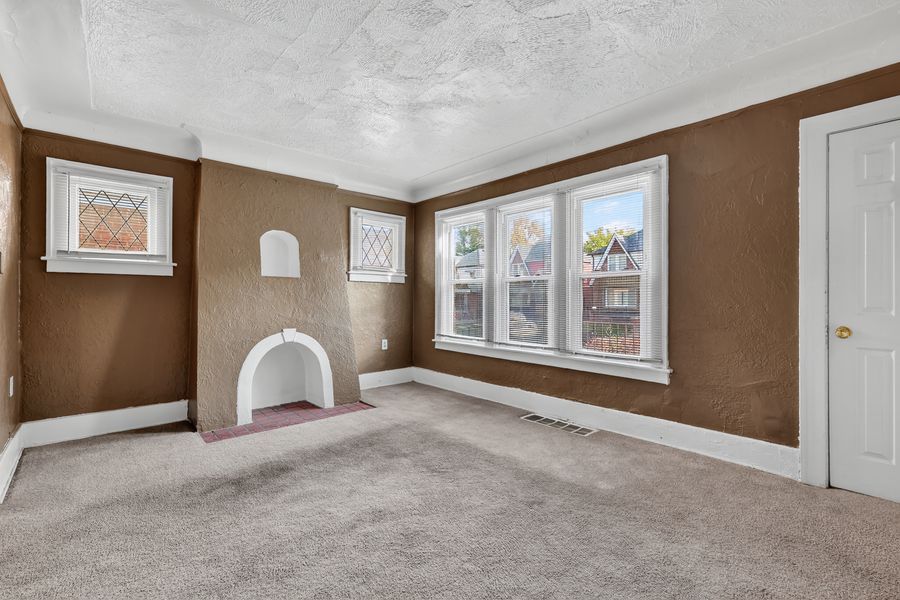 Cozy living room with brown walls, white fireplace, large windows, and neutral carpet flooring.
