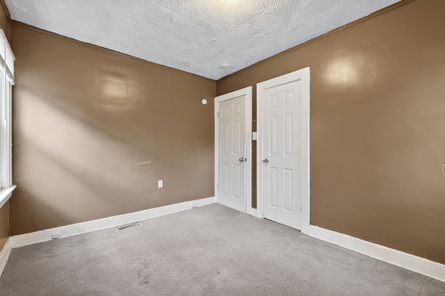 Empty bedroom with brown walls, white closet doors, carpet flooring, and textured ceiling.
