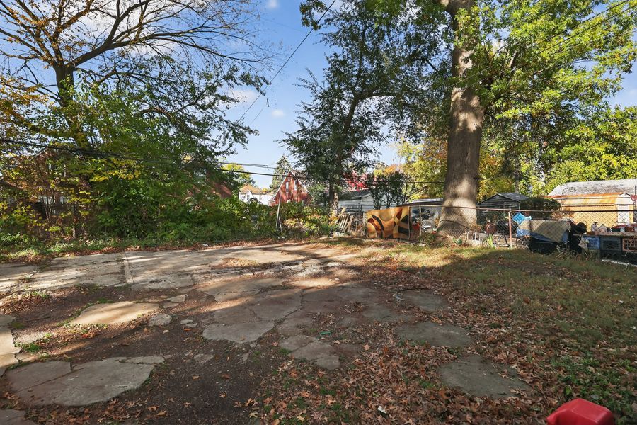 Stone patio surrounded by mature trees and lush greenery in a spacious backyard with natural landscaping.