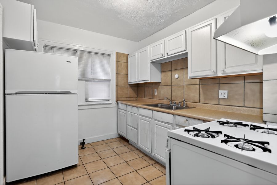 Bright kitchen with white cabinets, tile backsplash, white appliances, and beige tile flooring.