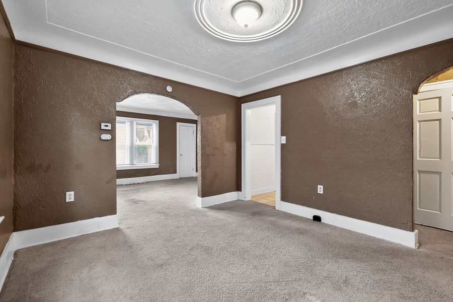 Spacious empty room with brown textured walls, carpet flooring, arched doorways, crown molding, and a decorative ceiling medallion.