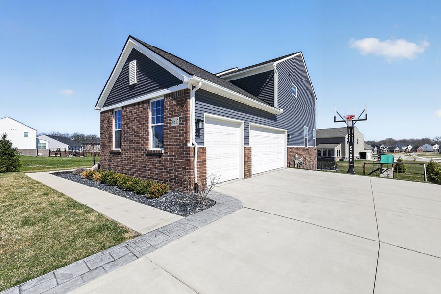 Charming two-story brick and gray siding home with a two-car garage and wide concrete driveway on a sunny day.