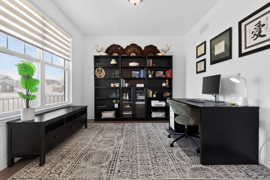 Elegant home office with black bookshelves, L-shaped desk, green chair, and large window overlooking greenery on patterned rug.